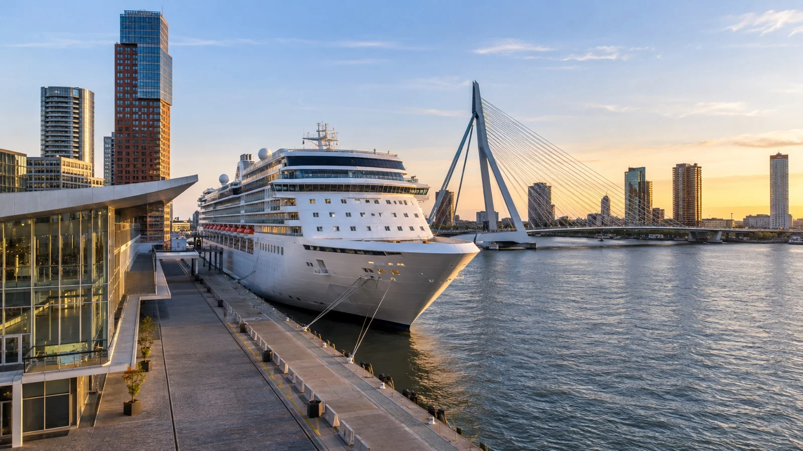 Rotterdam cruise terminal on Wilhelminapier with a large white cruise ship docked beside the Nieuwe Maas river and Erasmus Bridge