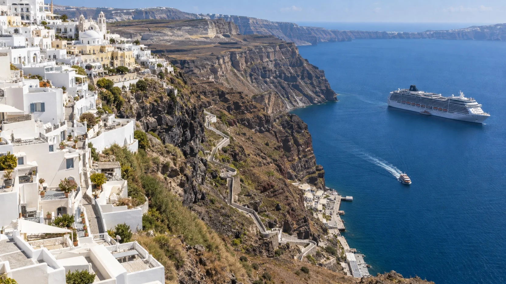Cruise ship and tender below the steep Santorini caldera cliff