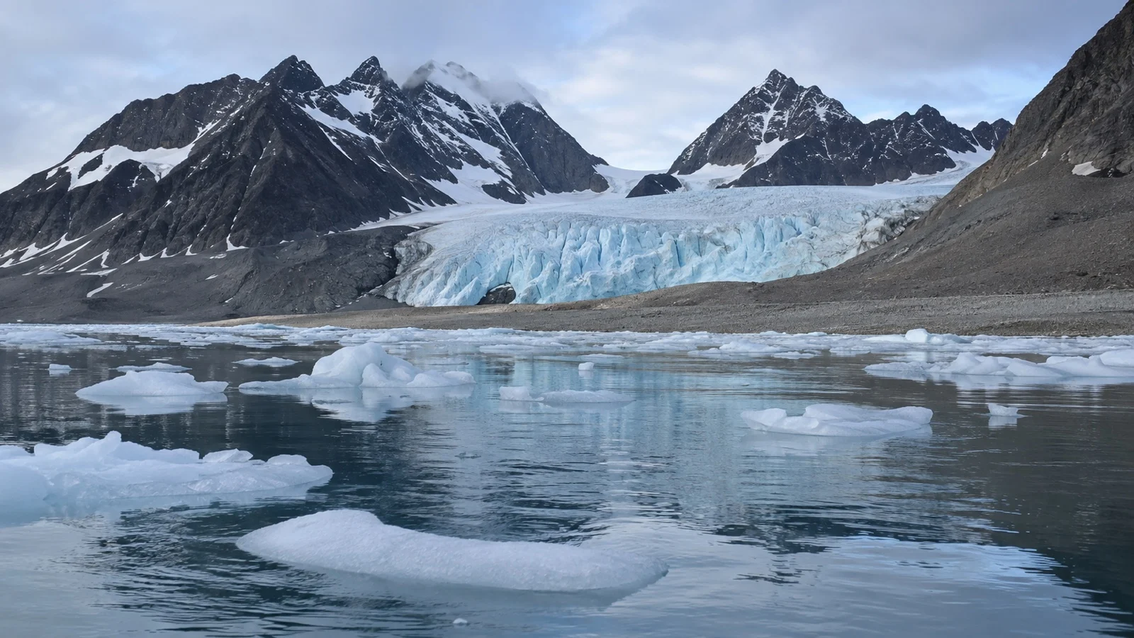 Remote Svalbard glacier and empty gravel shore with ice in the fjord
