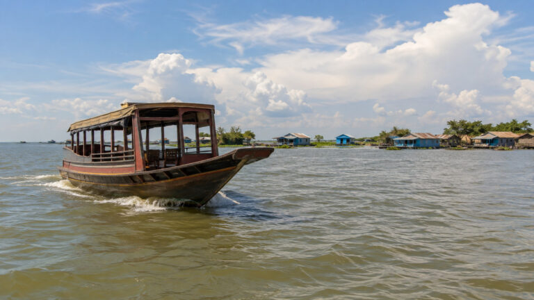 a small river cruise vessel crossing the open brown-green waters of Cambodia's Tonle Sap Lake under a wide sky