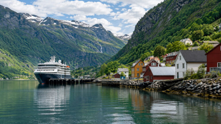 Small cruise ship at Vikoyri Norway fjord village landing with steep green mountains and colorful wooden houses, no people